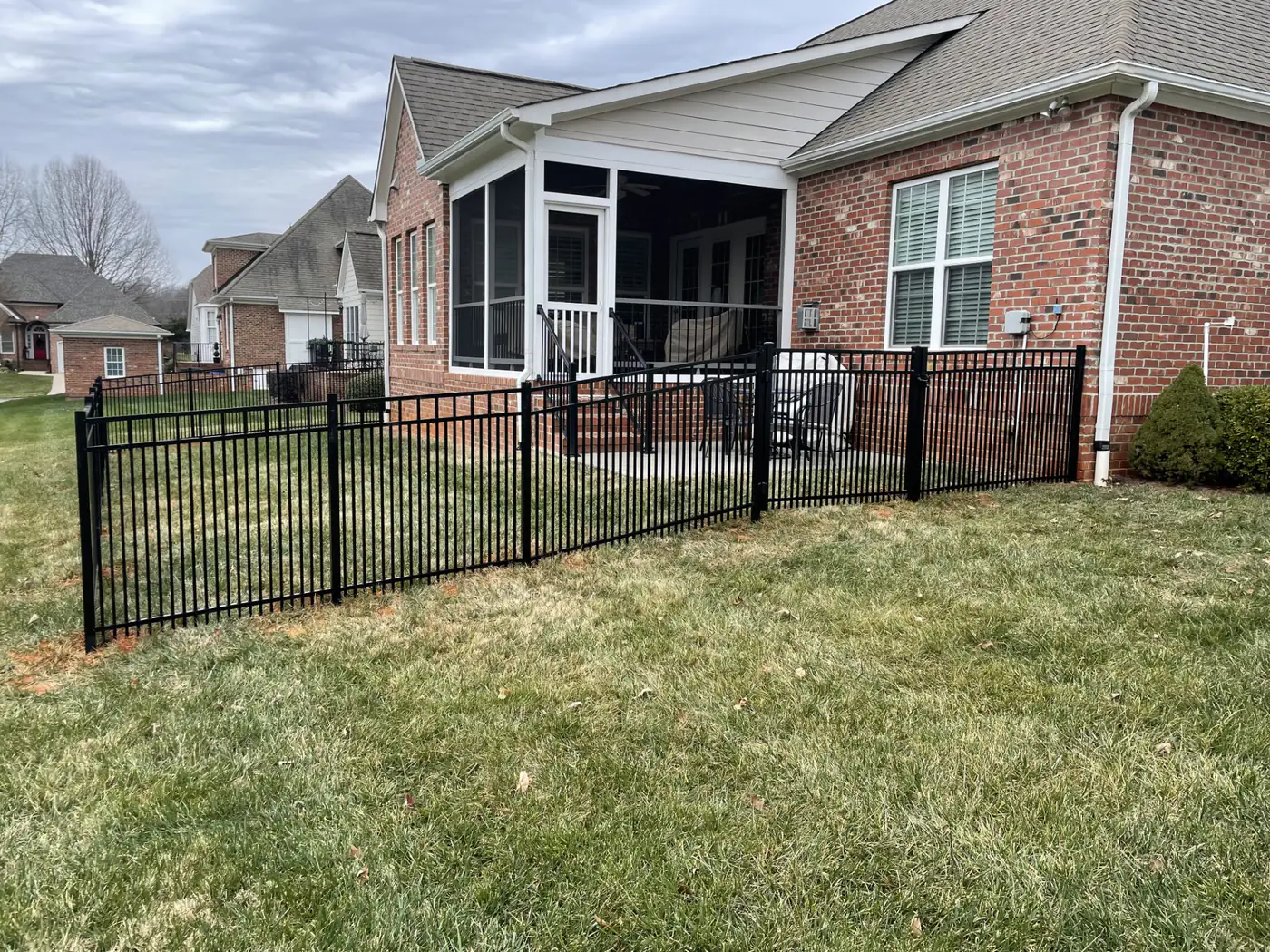 Black aluminum fence enclosing the rear yard of a brick home with a screened porch in Apex, NC