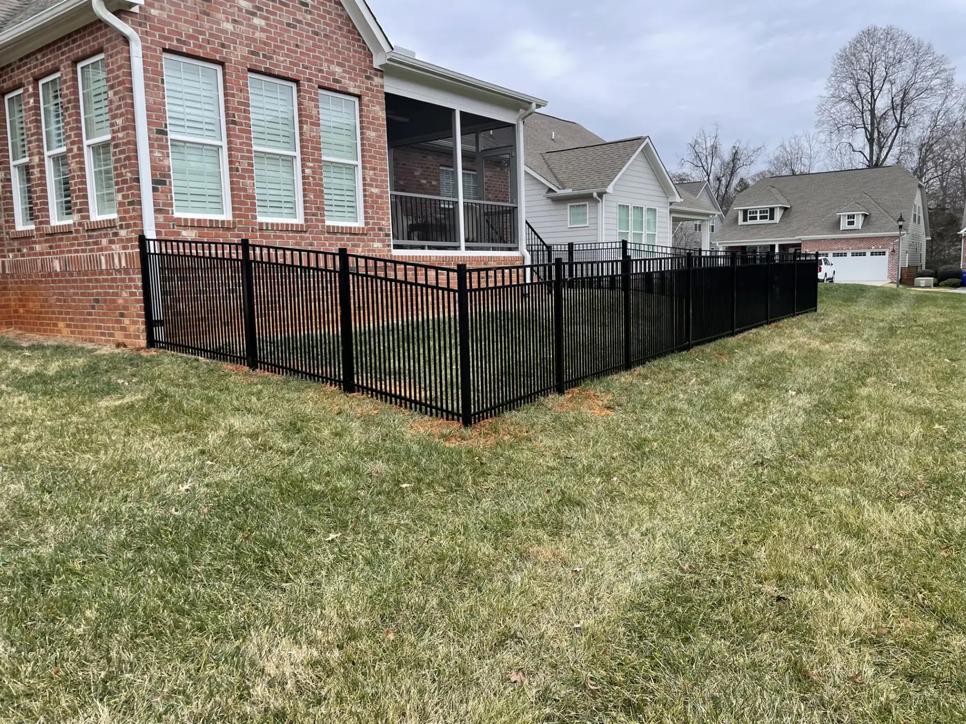 Black aluminum fence around a brick home with a screened porch