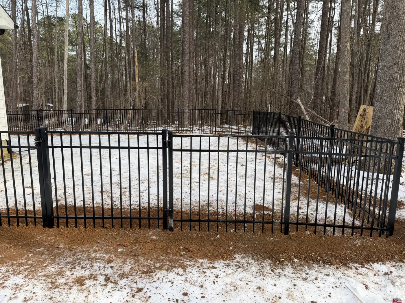 Black aluminum fence and gate installed among pines in winter