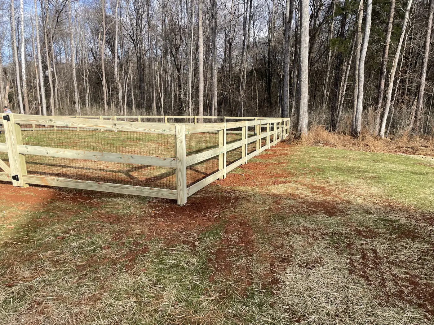 Split-rail farm fence with wire mesh backing and a wide gate on an open lot