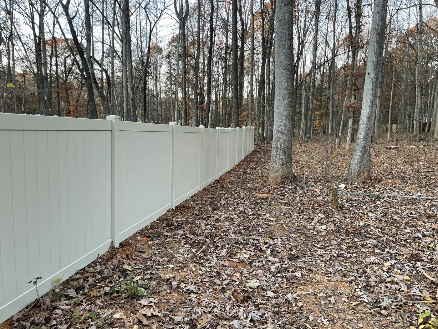 White vinyl privacy fence installed along a wooded tree line