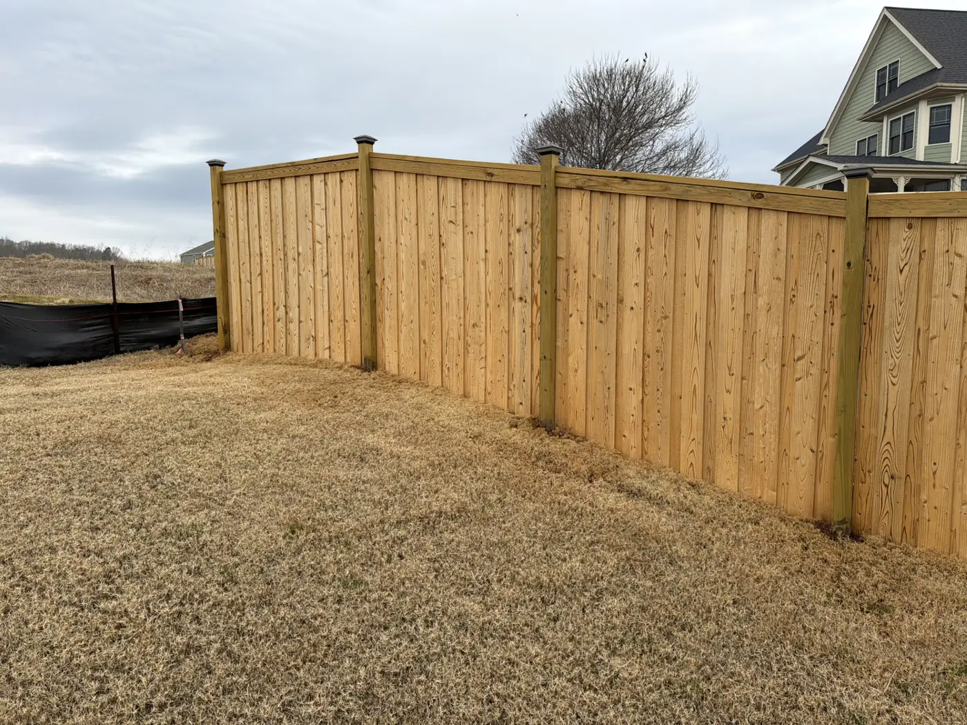 Cedar-tone cap-and-trim wood fence beside a newly built home
